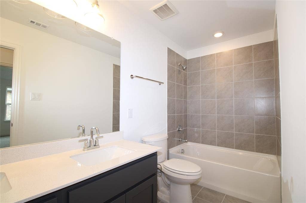 2603 Swallowtail Street, Melissa, TX 75454 Bathroom featuring a vanity with a white countertop and rectangular undermount sink, large wall-mounted mirror, brushed nickel faucet hardware, and a tub-shower combination with floor-to-ceiling tile surround