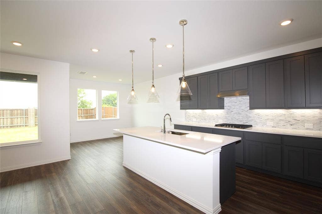 2603 Swallowtail Street, Melissa, TX 75454 Kitchen featuring dark-toned cabinetry, quartz countertops, a central island with a built-in sink, recessed lighting, and glass pendant fixtures