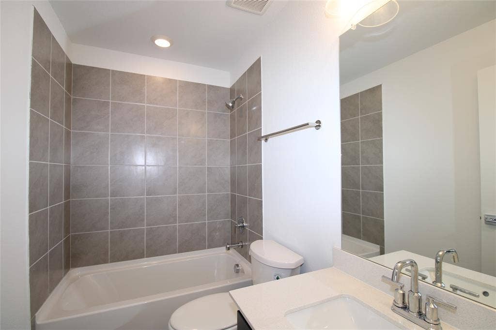 2603 Swallowtail Street, Melissa, TX 75454 Full-height tile shower surround with integrated tub, vanity featuring a light-toned solid surface countertop, undermount sink with dual-handle chrome faucet, and large wall-mounted mirror