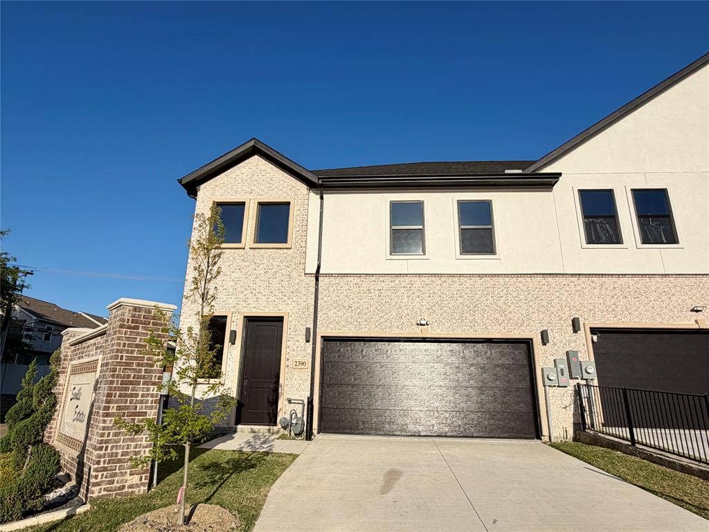2390 Usman Drive, Irving, TX 75062 Multi-level exterior featuring a light-toned brick and smooth stucco facade, dual-pane windows, a dark-finish panel entry door, and an attached two-car garage