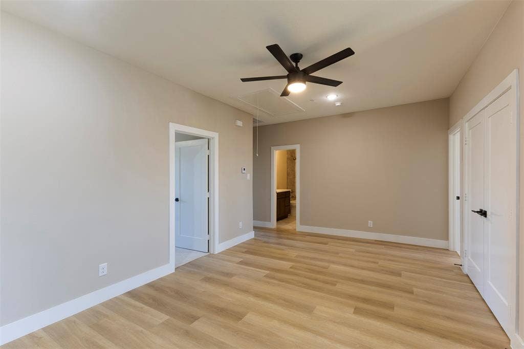 2390 Usman Drive, Irving, TX 75062 Interior space featuring wood-finish flooring, neutral wall color, matte black ceiling fan with integrated lighting, and multiple white paneled doors