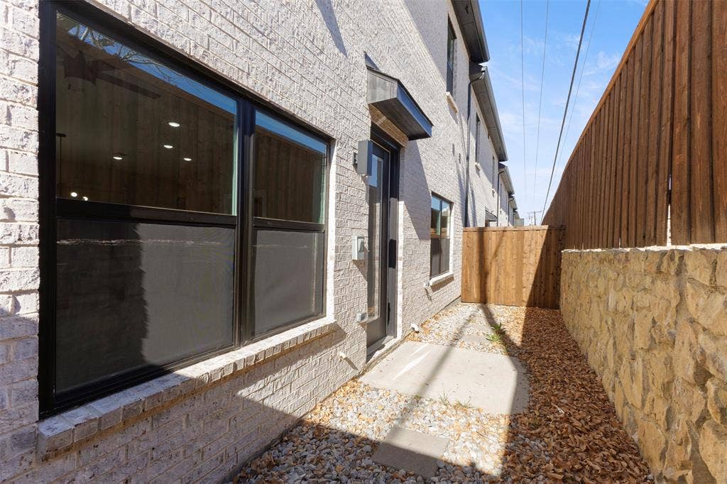 2390 Usman Drive, Irving, TX 75062 Light-colored brick exterior featuring oversized windows with black frames, a wood privacy fence, and a decorative natural stone retaining wall