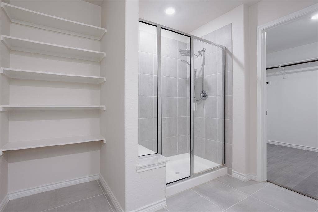 610 Overlook Point, Lavon, TX 75166 Walk-in shower featuring a glass enclosure, square tile surround, and adjustable handheld shower head, complemented by built-in wall shelving and large-format floor tile