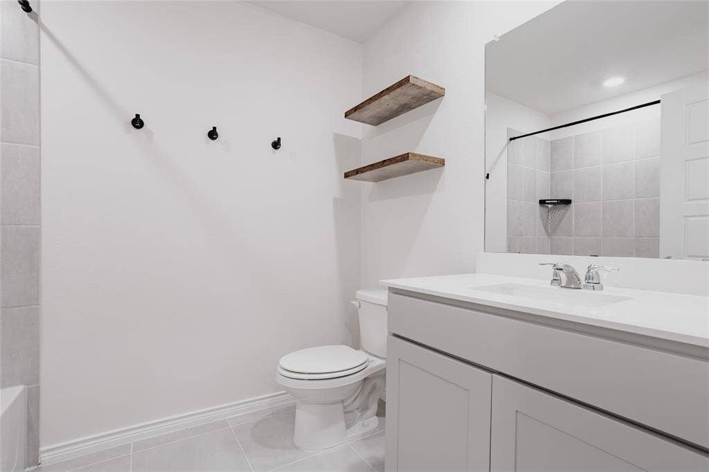 610 Overlook Point, Lavon, TX 75166 Bathroom featuring a vanity with a white countertop and undermount sink, wall-mounted wood-finish floating shelves, a large frameless mirror, and a tiled shower surround
