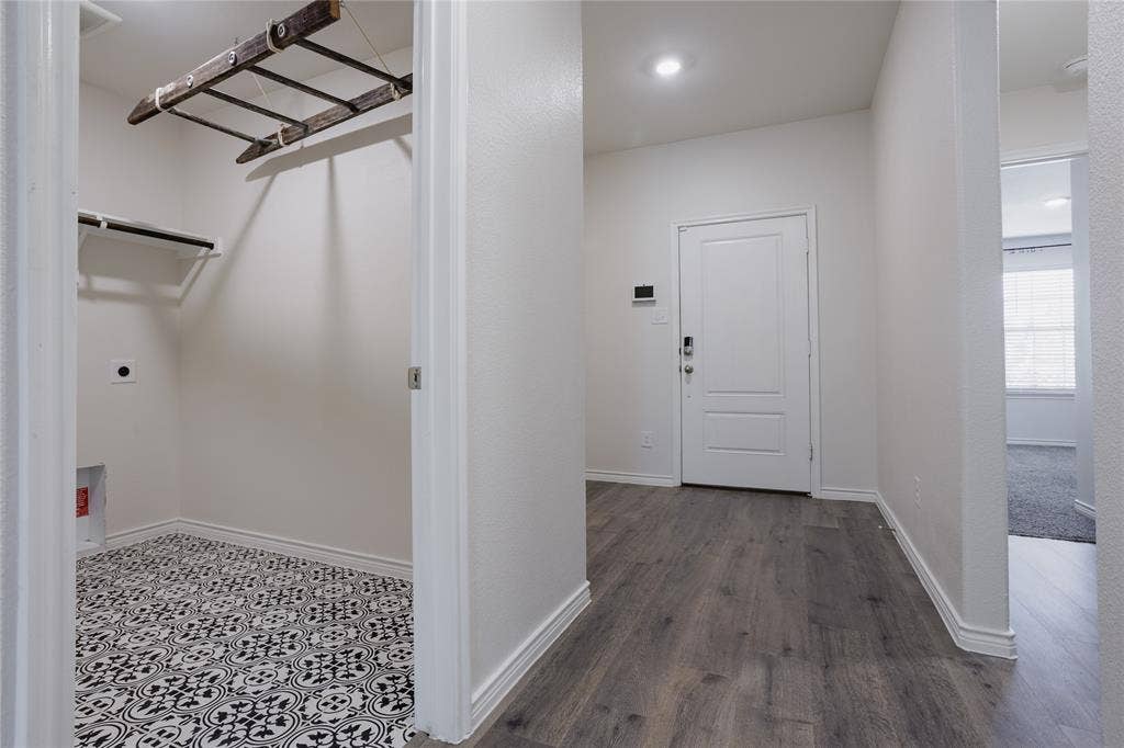 610 Overlook Point, Lavon, TX 75166 Laundry area featuring patterned tile flooring and a ceiling-mounted wooden drying rack, with wood-finish flooring in the hallway and a panelled entry door