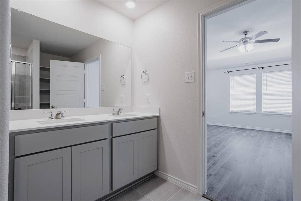 610 Overlook Point, Lavon, TX 75166 Dual-sink vanity with light-toned countertop, large wall-spanning mirror, grey cabinetry, and wood-finish flooring throughout the space