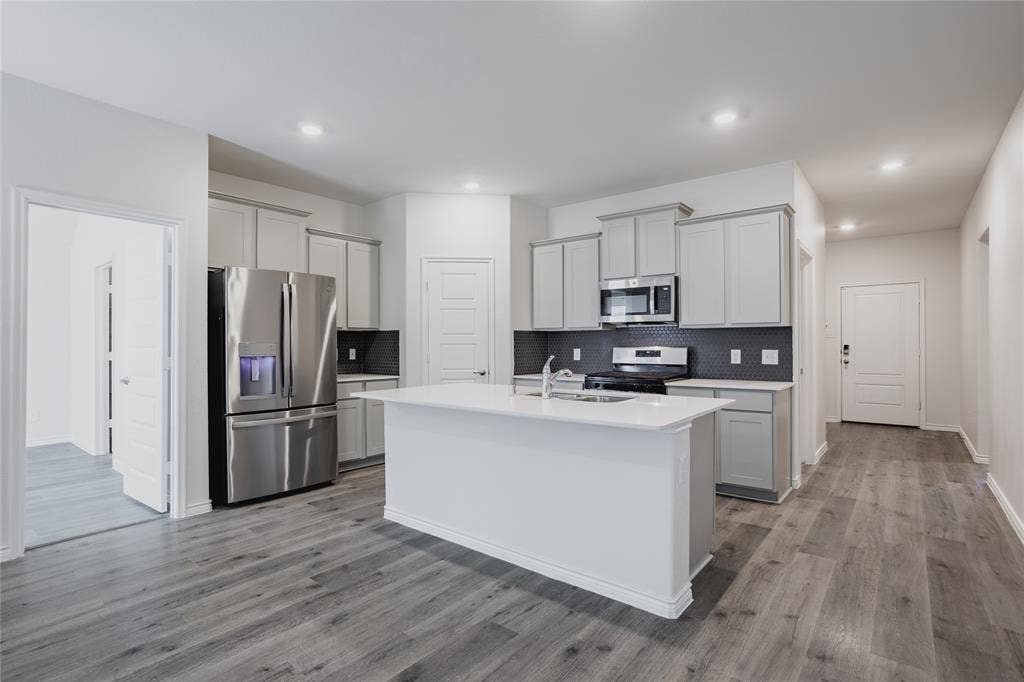 610 Overlook Point, Lavon, TX 75166 Kitchen featuring a central island with a quartz countertop, stainless steel appliances, light gray cabinetry, a dark tiled backsplash, and wood-finish flooring