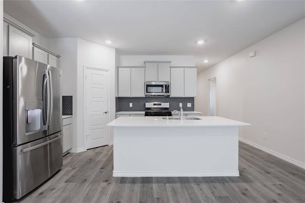 610 Overlook Point, Lavon, TX 75166 Kitchen featuring a central island with a solid surface countertop, stainless steel appliances, Shaker-style cabinetry, a geometric tile backsplash, and wood-finish flooring