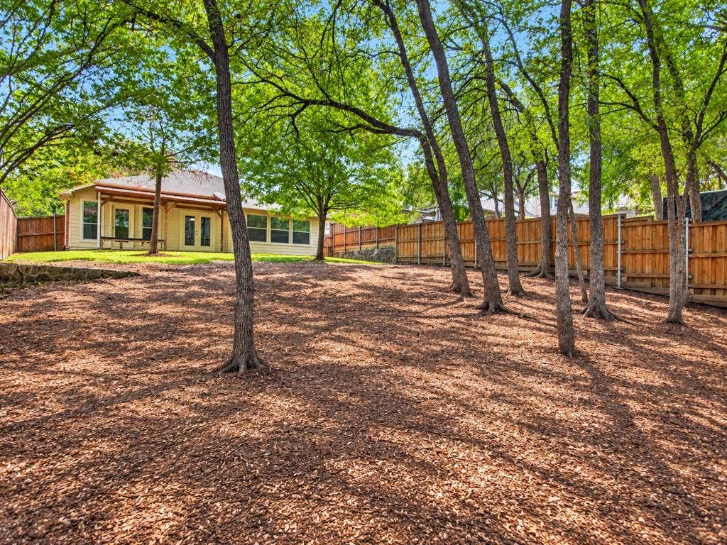 2691 Eganridge Lane, Rockwall, TX 75087 Expansive backyard featuring mature trees, wood privacy fencing, a natural stone retaining wall, and a covered patio