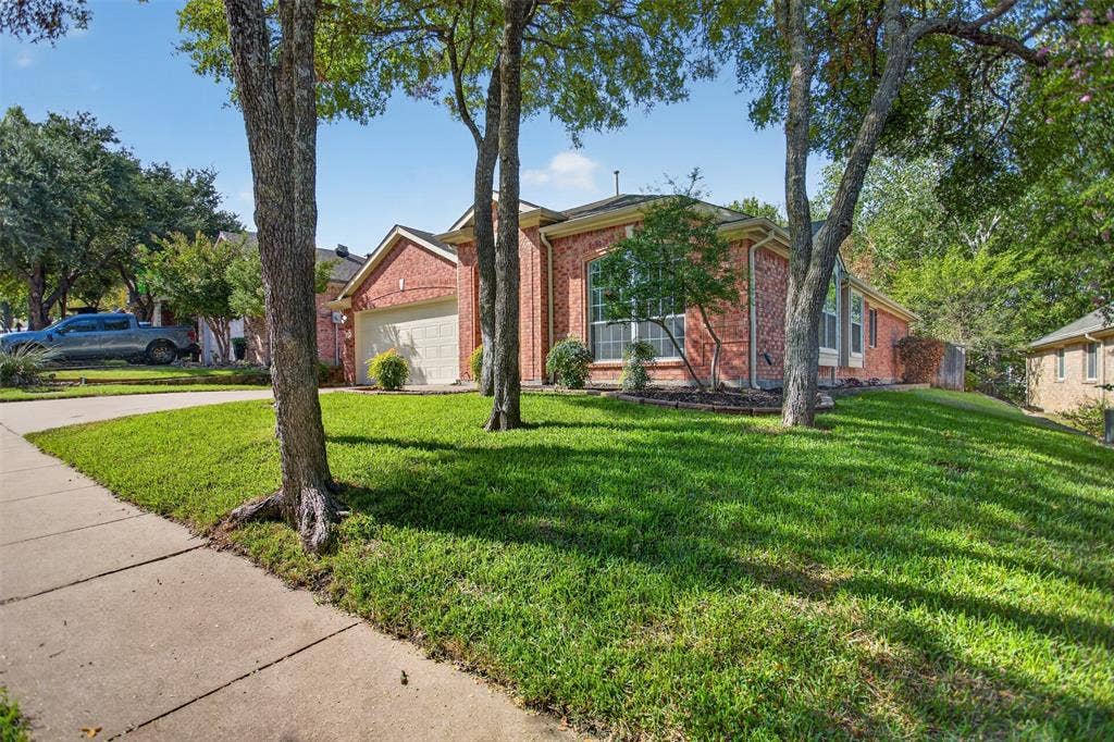 2691 Eganridge Lane, Rockwall, TX 75087 Brick exterior featuring a multi-gabled roofline, an attached two-car garage, large grid-pane windows, and a landscaped front yard with mature trees
