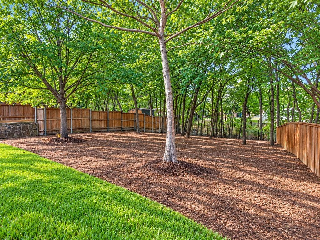 2691 Eganridge Lane, Rockwall, TX 75087 Backyard featuring mature trees, a manicured lawn, wood-panel fencing, and stone retaining wall