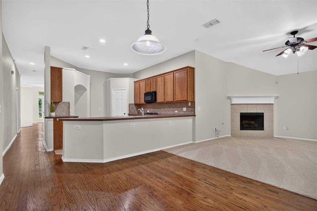 2691 Eganridge Lane, Rockwall, TX 75087 Open-concept area featuring wood-finish flooring, a kitchen with cabinetry and a breakfast bar, vaulted ceilings, and a fireplace with a tile surround