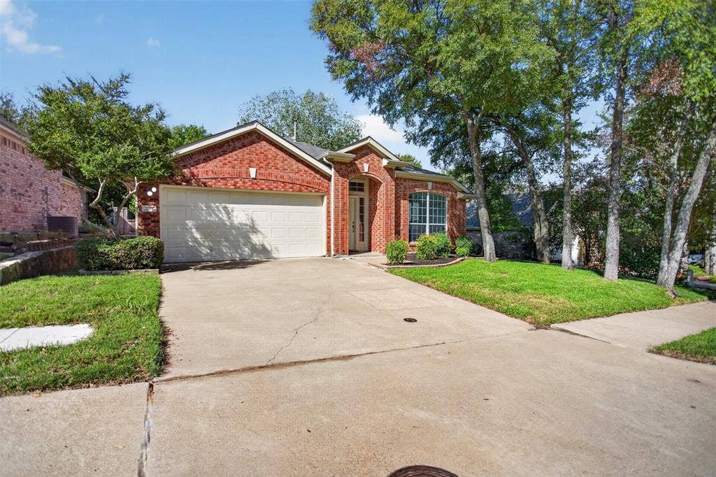 2691 Eganridge Lane, Rockwall, TX 75087 Single-story brick exterior featuring a front-facing attached two-car garage, arched entryway, and mature trees situated on a landscaped lot