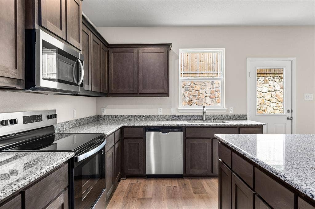 6307 Crosswood Lane, Dallas, TX 75241 Kitchen with appliances with stainless steel finishes, light wood-style flooring, dark brown cabinetry, and light stone counters