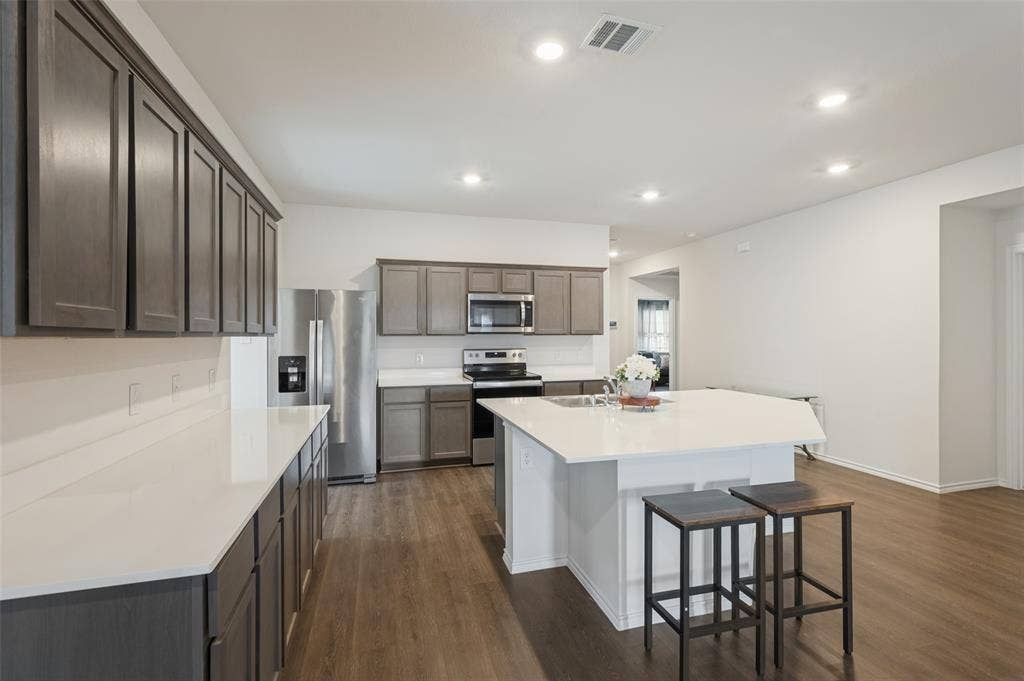 Kitchen featuring dark-toned cabinetry, solid-surface countertops, a center island, stainless steel appliances, and wood-finish flooring