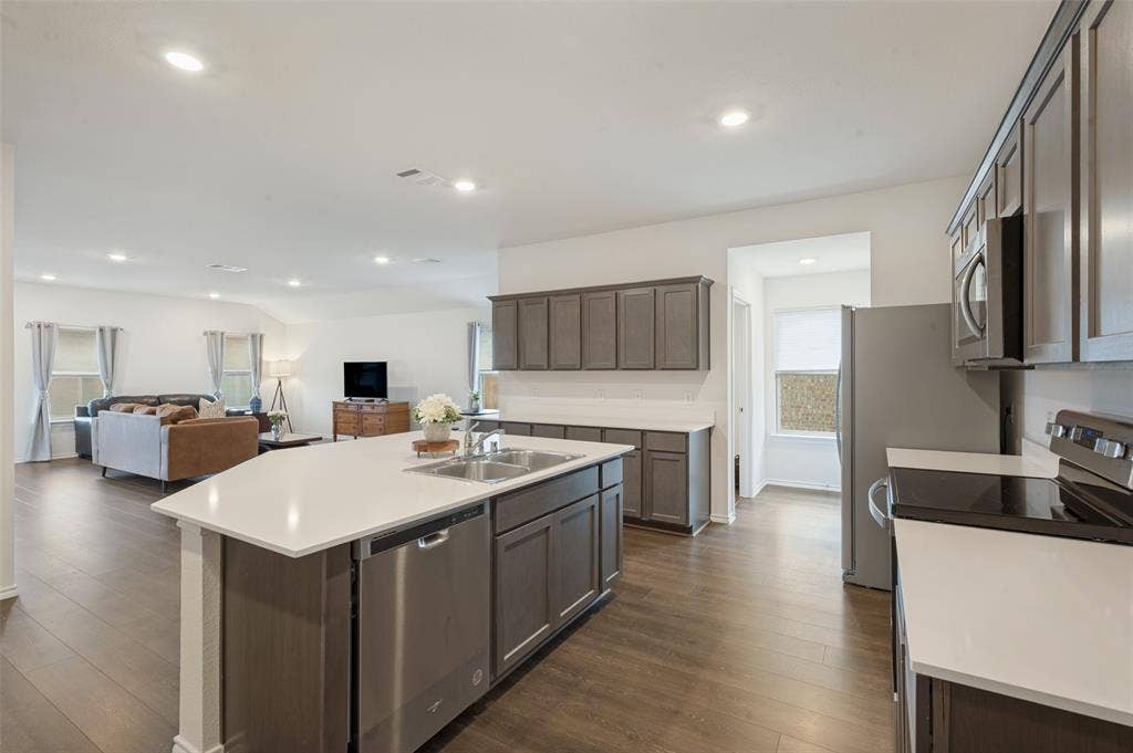 Kitchen featuring a central island with a double-basin sink, quartz countertops, dark-finish cabinetry, stainless steel dishwasher, and wood-finish flooring