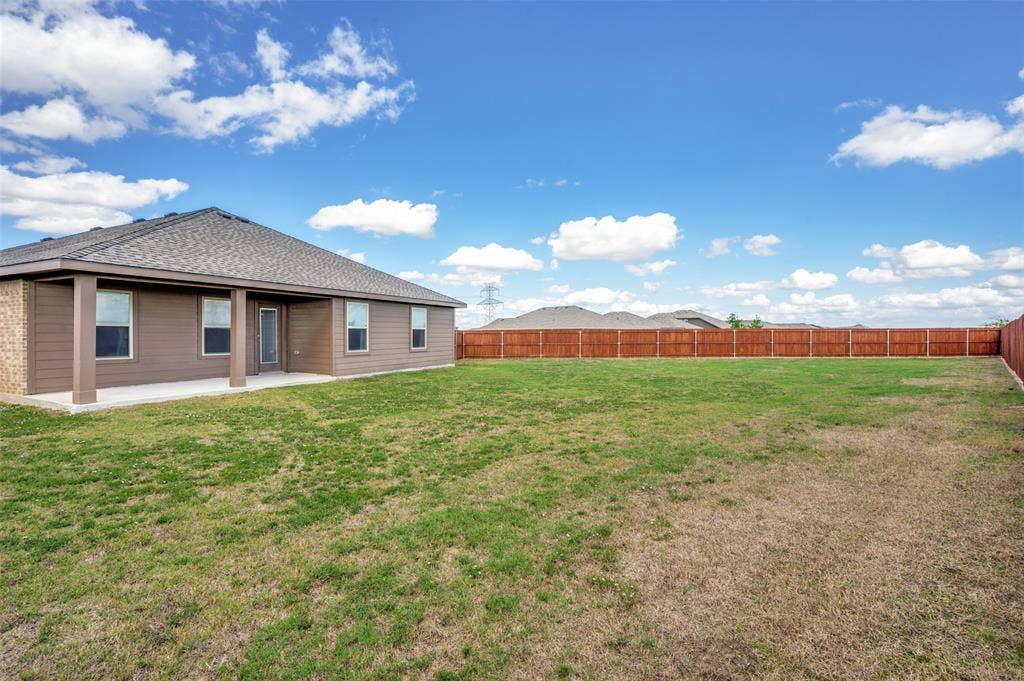 Spacious backyard featuring a concrete covered patio, horizontal wood-style siding, and full perimeter wood fencing