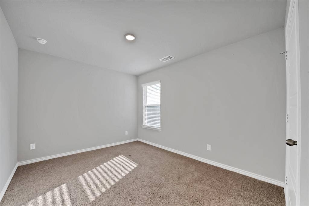 Neutral interior space featuring carpeting, smooth-finish walls, a single-pane window with horizontal blinds, and a solid-panel door with a metallic knob