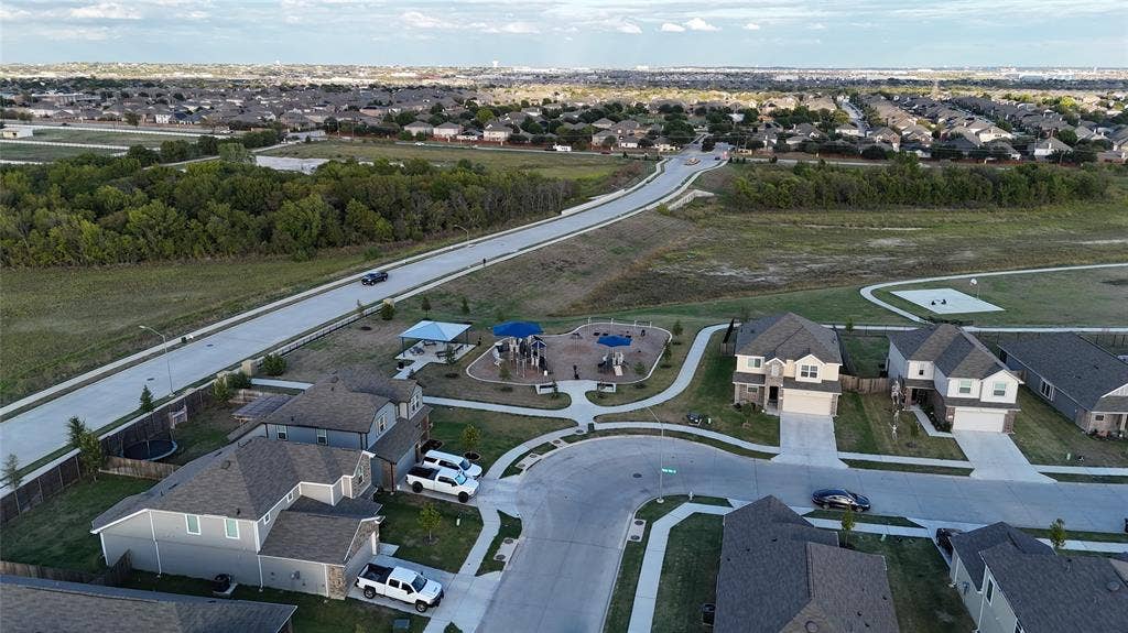 Aerial perspective of a neighborhood featuring concrete sidewalks, residential asphalt streets, landscaped open green space, and a community playground area with permanent shade structures