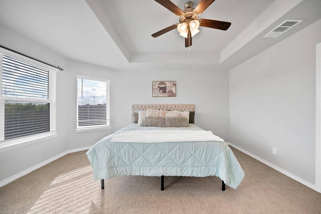 Room featuring a tray ceiling, ceiling fan with integrated lighting, and dual windows