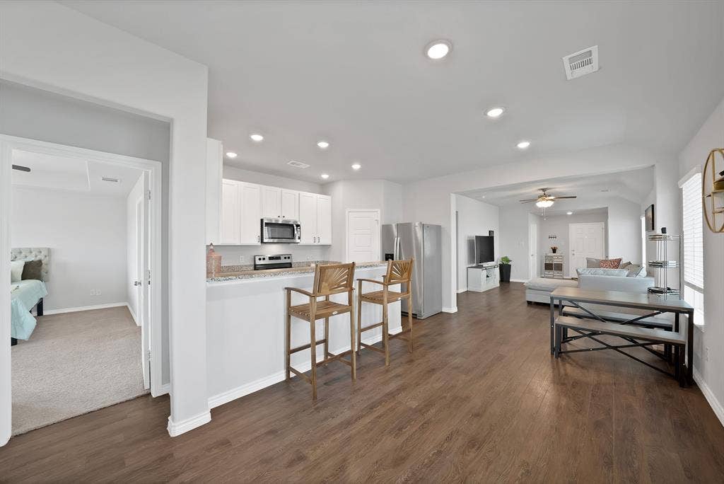 Kitchen featuring white shaker-style cabinetry, stone-finish countertops, stainless steel appliances, recessed lighting, and wood-finish flooring