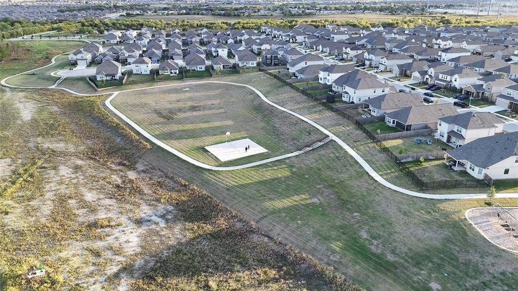 Aerial view of communal recreation space featuring a concrete basketball court, paved walking trails, and open green space