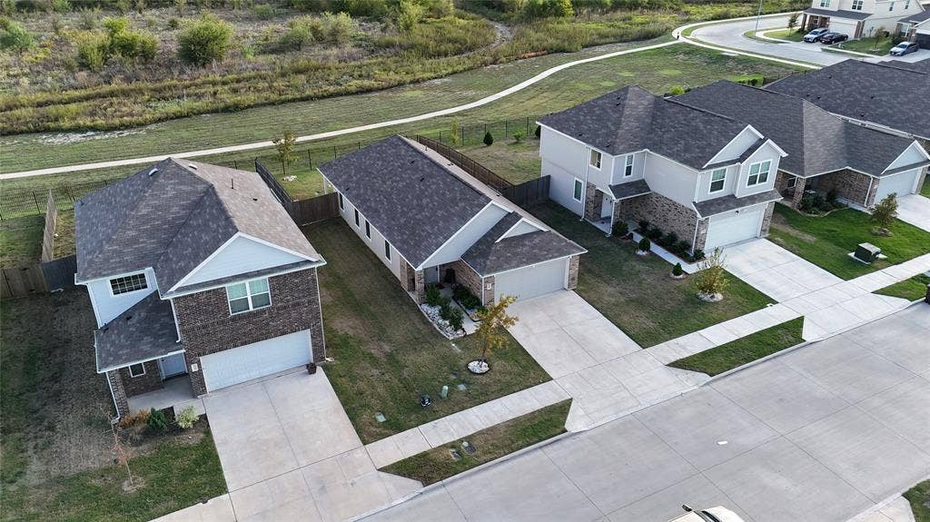 Aerial perspective of residential exteriors featuring mixed brick and siding facades, shingled roofing, concrete driveways, and backyards bordered by a winding trail