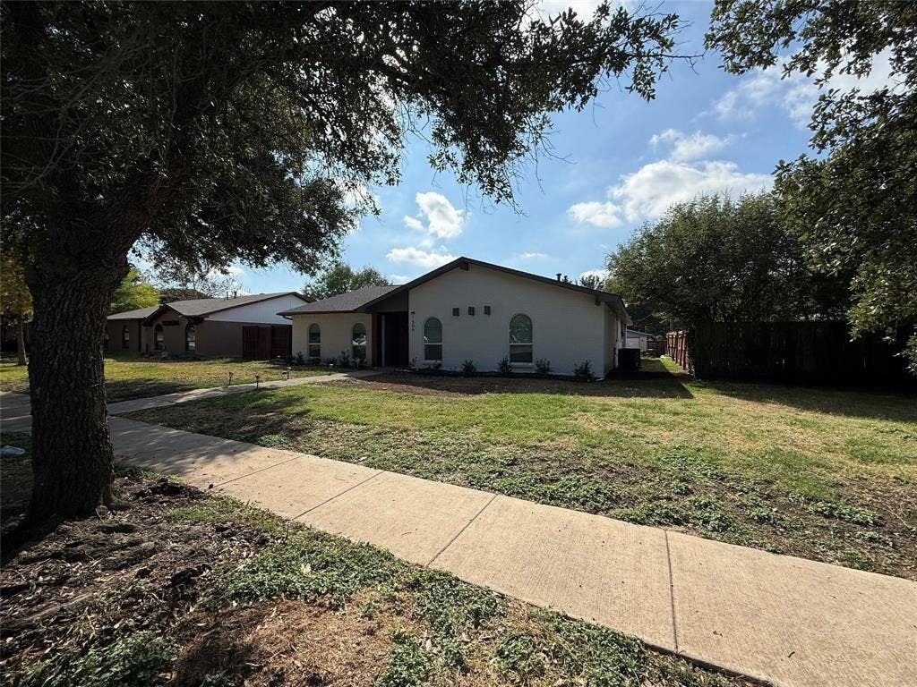 1506 W Spring Creek Parkway, Plano, TX 75023 Single-story residence featuring a light-toned exterior, arched windows, and a composition shingle roof, set on a lot with mature trees