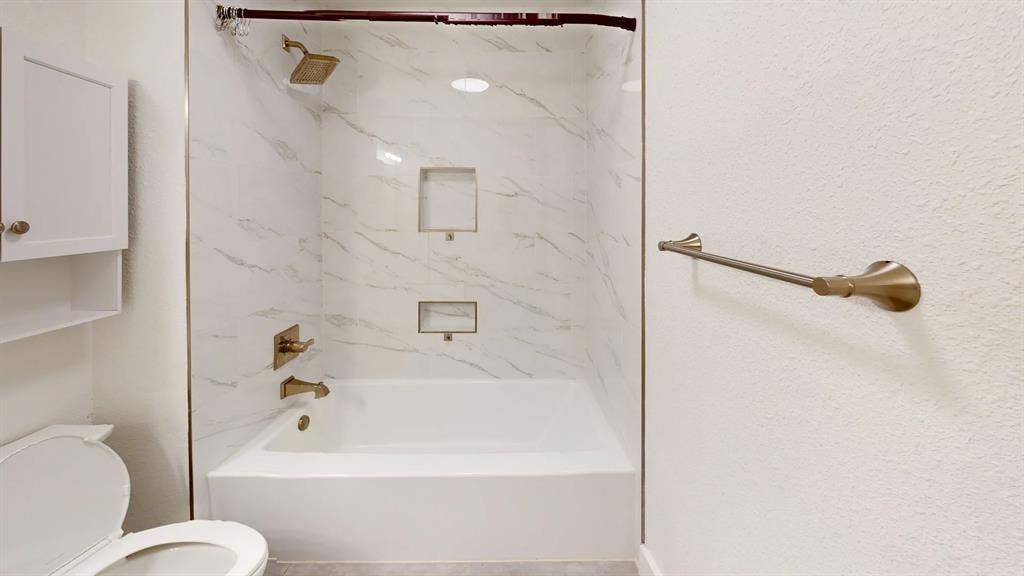 1506 W Spring Creek Parkway, Plano, TX 75023 Bathtub and shower combination featuring stone-finish wall surround, dual built-in recessed niches, and metallic-finish hardware