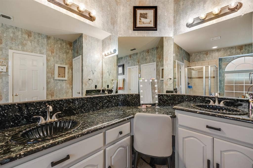 Bathroom featuring a stall shower, two vanities, and wallpapered walls