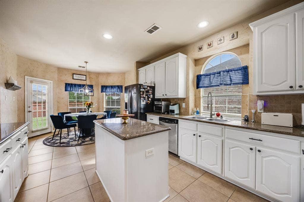 Kitchen featuring a kitchen island, tasteful backsplash, white cabinets, dark stone countertops, and light tile patterned floors