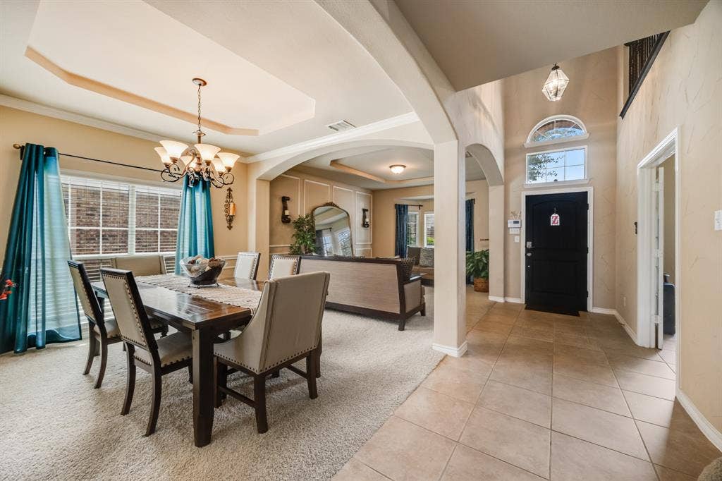 Dining area with a chandelier, light tile patterned floors, light colored carpet, and a tray ceiling