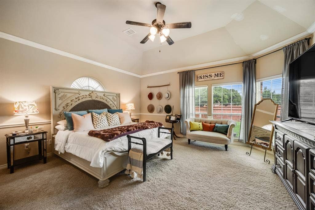 Bedroom with multiple windows, carpet flooring, ceiling fan, ornamental molding, and a raised ceiling