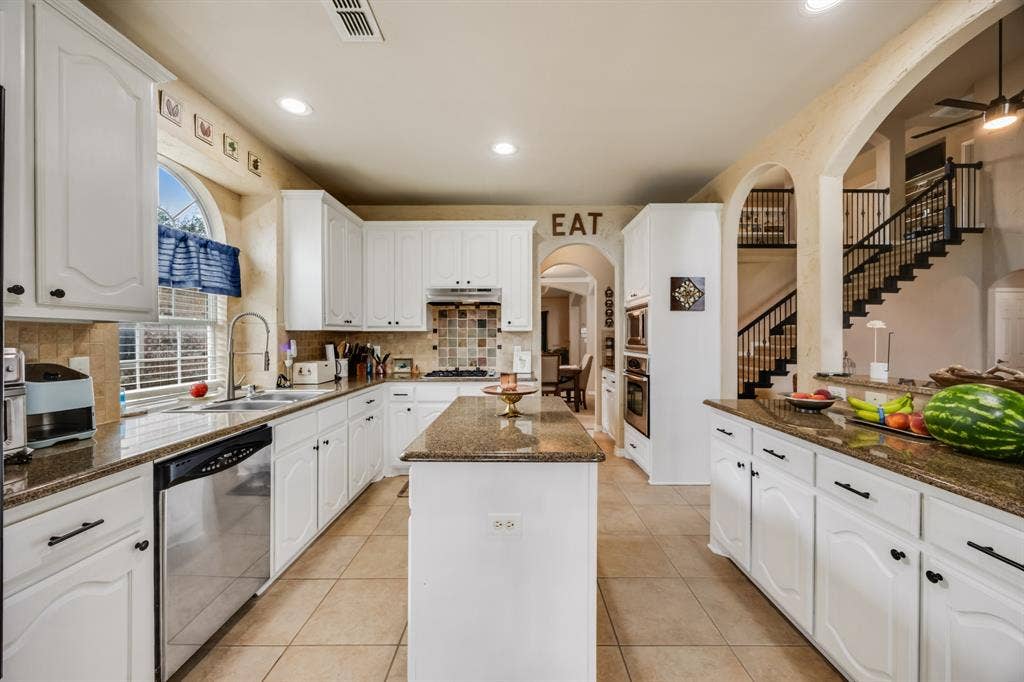 Kitchen featuring arched walkways, dark stone counters, white cabinets, light tile patterned floors, and backsplash
