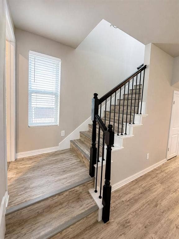 3704 Banton Street, Rowlett, TX 75089 Staircase featuring wood-finish flooring, white risers, black metal balusters, and a dark stained wood handrail