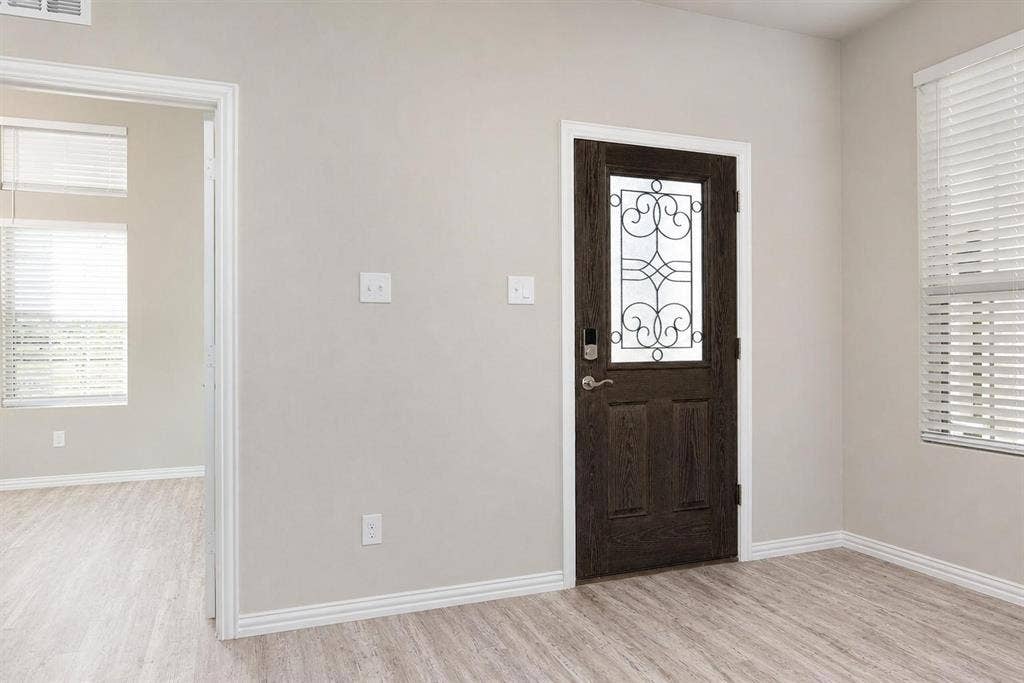 3704 Banton Street, Rowlett, TX 75089 Dark-finished wood entry door featuring decorative iron grillwork, horizontal wood-finish flooring, and window blinds