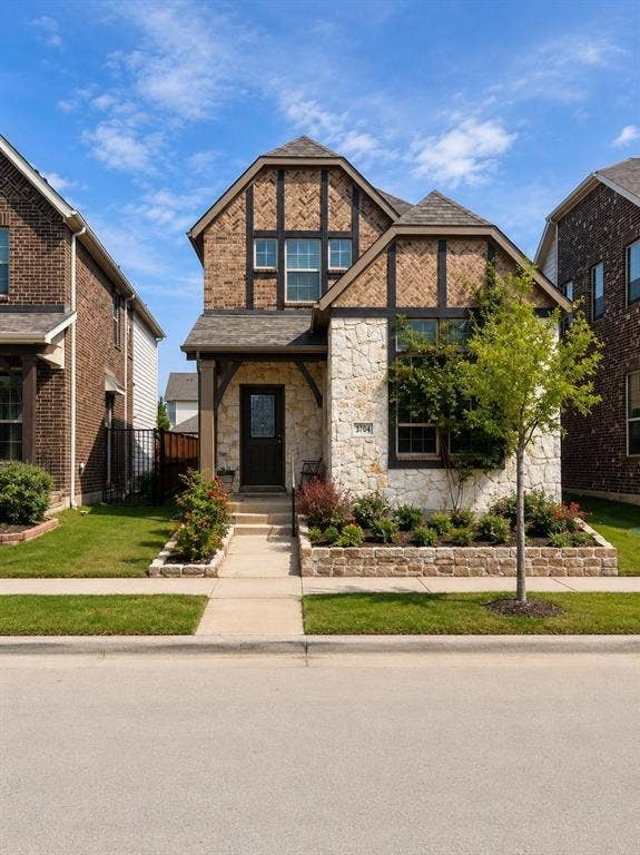 3704 Banton Street, Rowlett, TX 75089 Tudor-style exterior featuring stone veneer, half-timbered gables, a covered entry, and custom raised stone garden beds