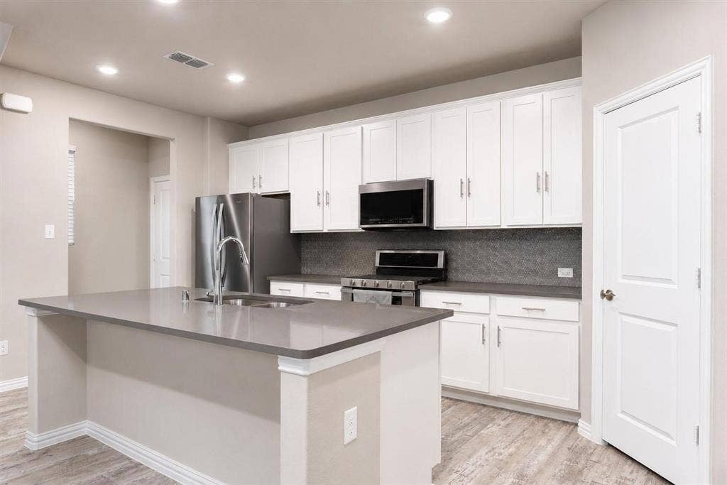 3704 Banton Street, Rowlett, TX 75089 Kitchen featuring white shaker-style cabinetry, quartz countertops, a central island with an integrated sink, stainless steel appliances, and wood-finish flooring