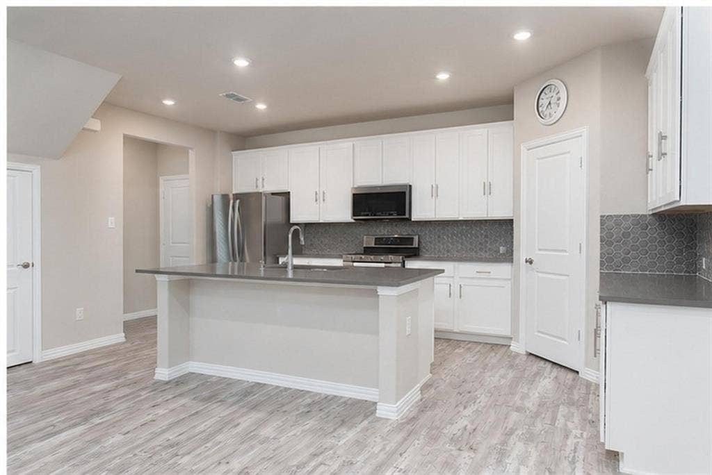 3704 Banton Street, Rowlett, TX 75089 Kitchen featuring white cabinetry, solid-surface countertops, a center island with a stainless steel sink, hexagonal tile backsplash, and wood-finish flooring