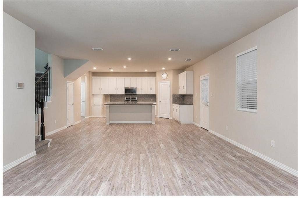 3704 Banton Street, Rowlett, TX 75089 Open-concept interior featuring wood-finish flooring, recessed lighting, white cabinetry, a center island, and a staircase with a dark-finished handrail