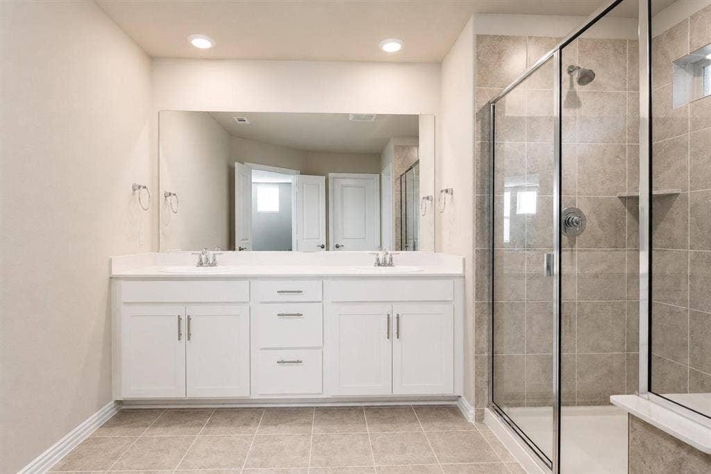 3704 Banton Street, Rowlett, TX 75089 Double vanity with white cabinetry, solid surface countertop, expansive wall mirror, and walk-in shower featuring tiled walls and a glass enclosure