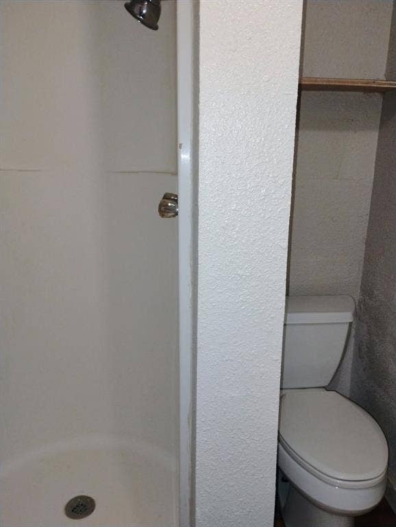 412 N Saint Augustine Drive, Dallas, TX 75217 Shower stall with integrated surround, chrome fixtures, white porcelain toilet, and built-in shelving