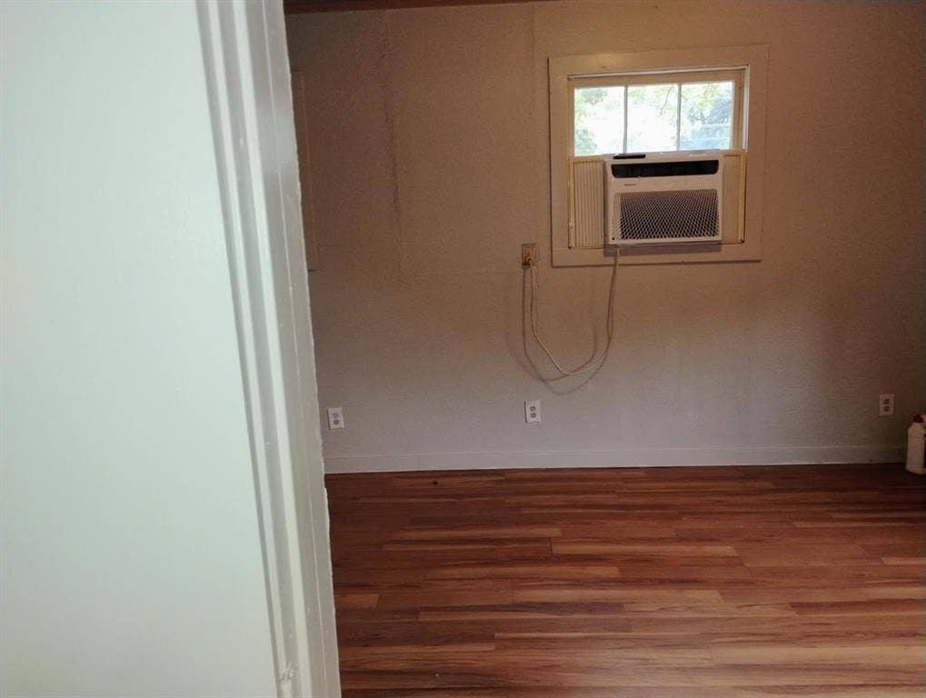 412 N Saint Augustine Drive, Dallas, TX 75217 Interior room featuring wood-finish flooring, a white-framed single-pane window, and a wall-mounted air conditioning unit