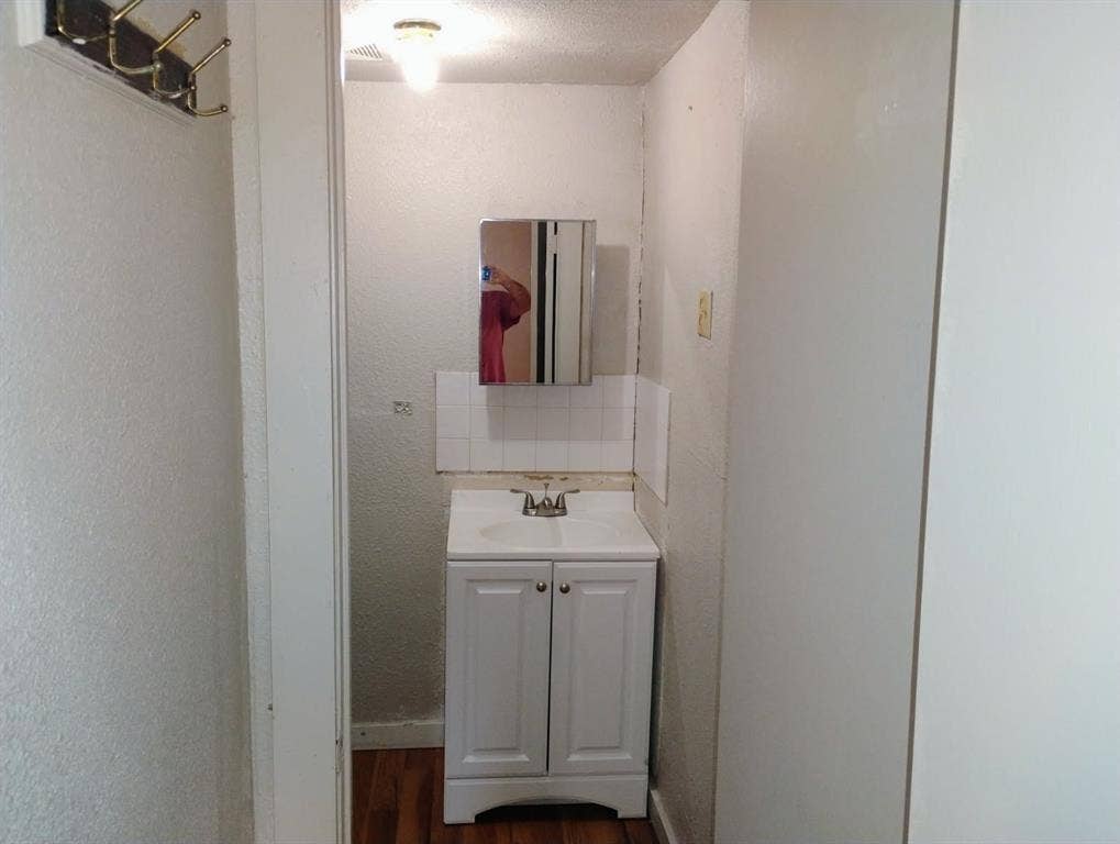 412 N Saint Augustine Drive, Dallas, TX 75217 White vanity cabinet with an integrated basin, chrome-finish dual-handle faucet, mirrored medicine cabinet, and wood-finish flooring