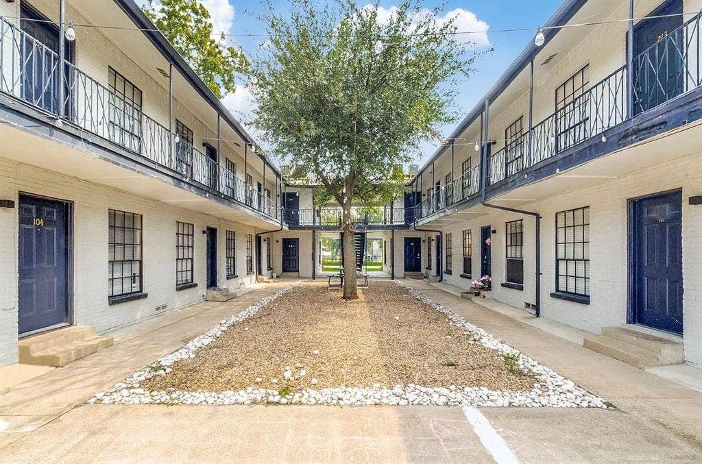 5317 Junius Street, #212, Dallas, TX 75214 Exterior courtyard featuring white brick architecture, multi-level metal railings, grid-pattern windows, and a central gravel landscape design