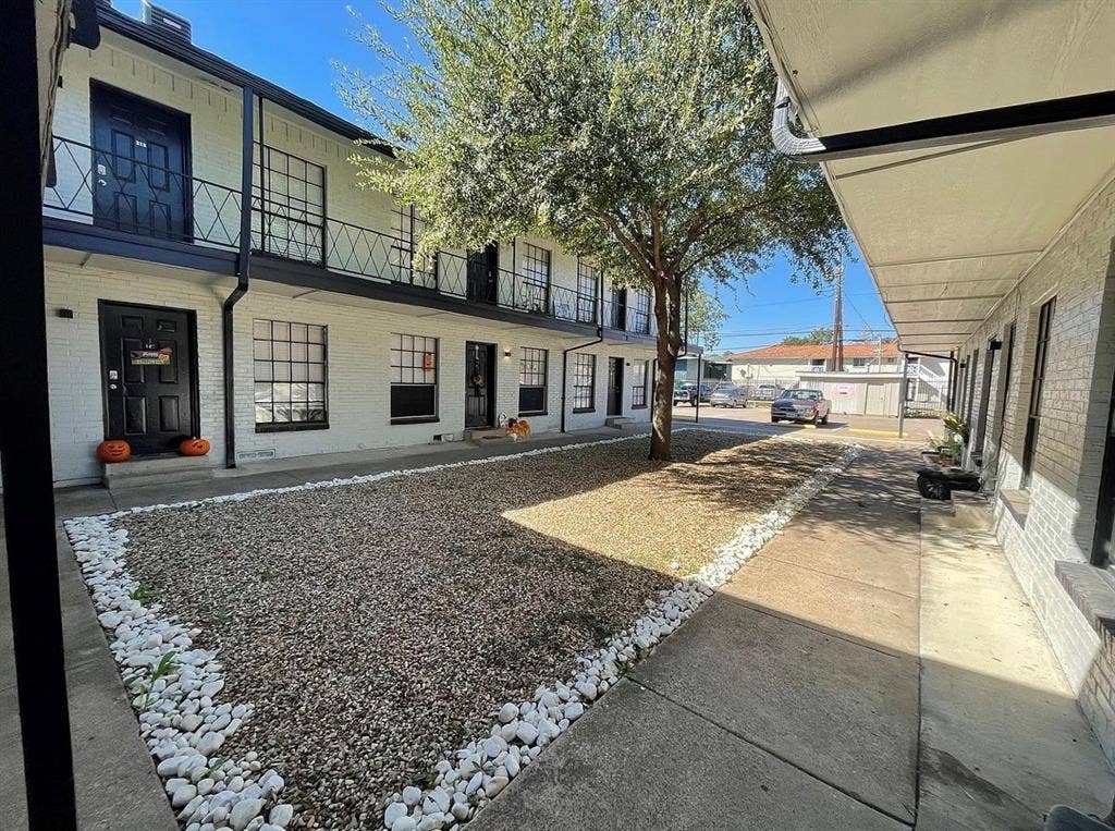 5317 Junius Street, #212, Dallas, TX 75214 Multi-story exterior featuring painted brick, black metal balcony railings, a gravel courtyard with stone border, and concrete walkways