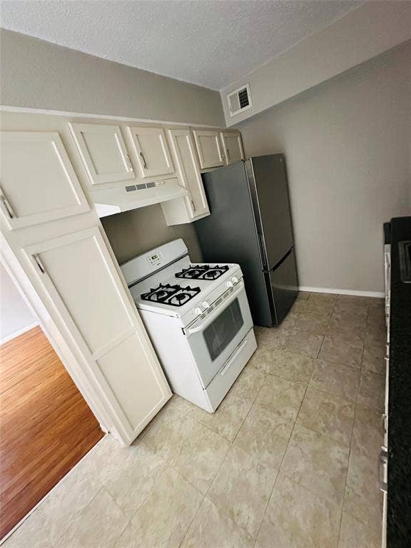 5317 Junius Street, #212, Dallas, TX 75214 Kitchen featuring white cabinetry, a freestanding gas range, a stainless steel refrigerator, and stone-finish tile flooring