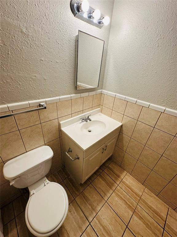 5317 Junius Street, #212, Dallas, TX 75214 Vanity cabinet with an integrated sink and chrome faucet, mounted medicine cabinet, three-light fixture, and ceramic tile wainscoting