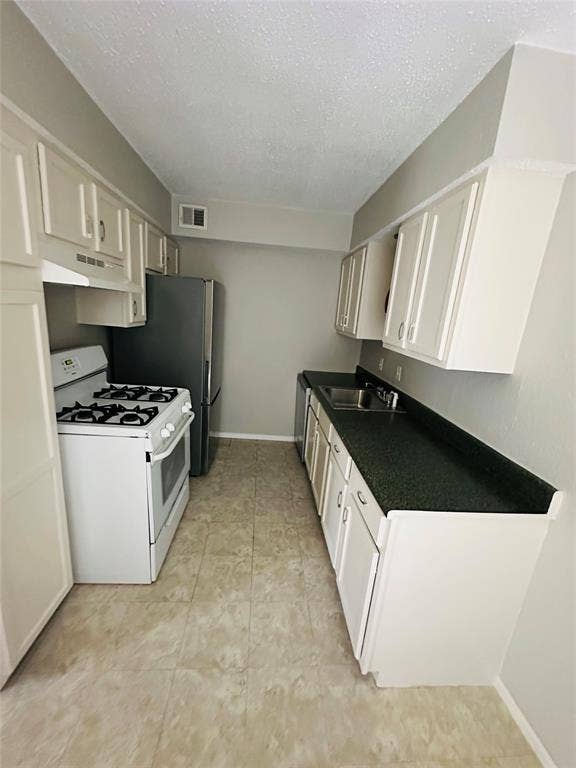 5317 Junius Street, #212, Dallas, TX 75214 Galley kitchen featuring white cabinetry, dark countertops, a stainless steel sink, a four-burner gas range, and ceramic tile flooring