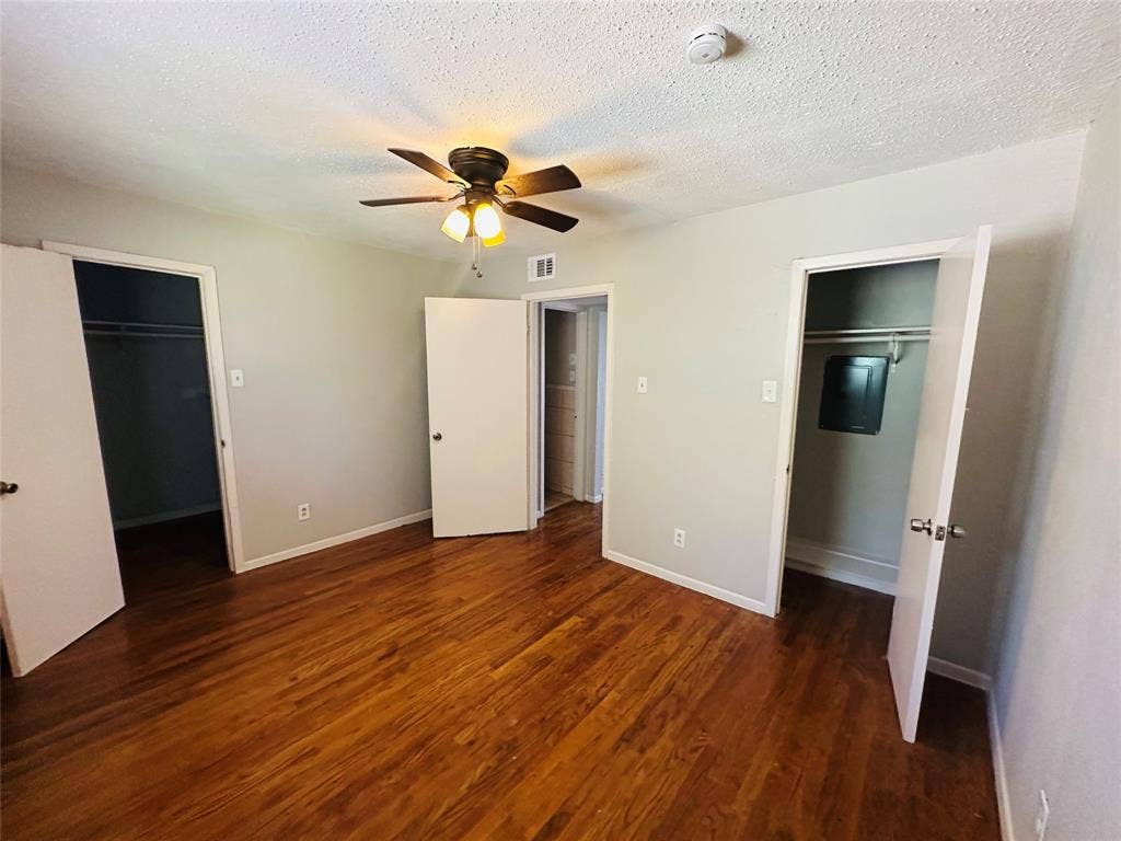 5317 Junius Street, #212, Dallas, TX 75214 Room featuring wood-finish flooring, two closets with built-in shelving, and a ceiling-mounted light fixture with a fan